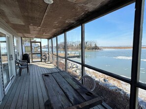 Eine überdachte Terrasse mit Blick auf einen zugefrorenen See, Holzbanken und einem Tisch.