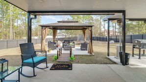 Een overdekt terras met een pergola, zithoek en barbecue.