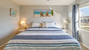 A hotel room with a bed, two bedside tables with lamps, a ceiling fan, a beach-themed painting, and a window with curtains. - Sebring Fairway Villa Golf, Lake, Track, & Pools (Sebring)