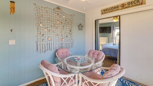 A room with a round glass table surrounded by wicker chairs, a wall decorated with a net of seashells, and a sign reading "WELCOME TO OUR DECK". - Sebring Fairway Villa Golf, Lake, Track, & Pools (Sebring)
