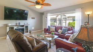 A living room with a television, leather sofas, a glass coffee table, and a ceiling fan. - Sebring Fairway Villa Golf, Lake, Track, & Pools (Sebring)
