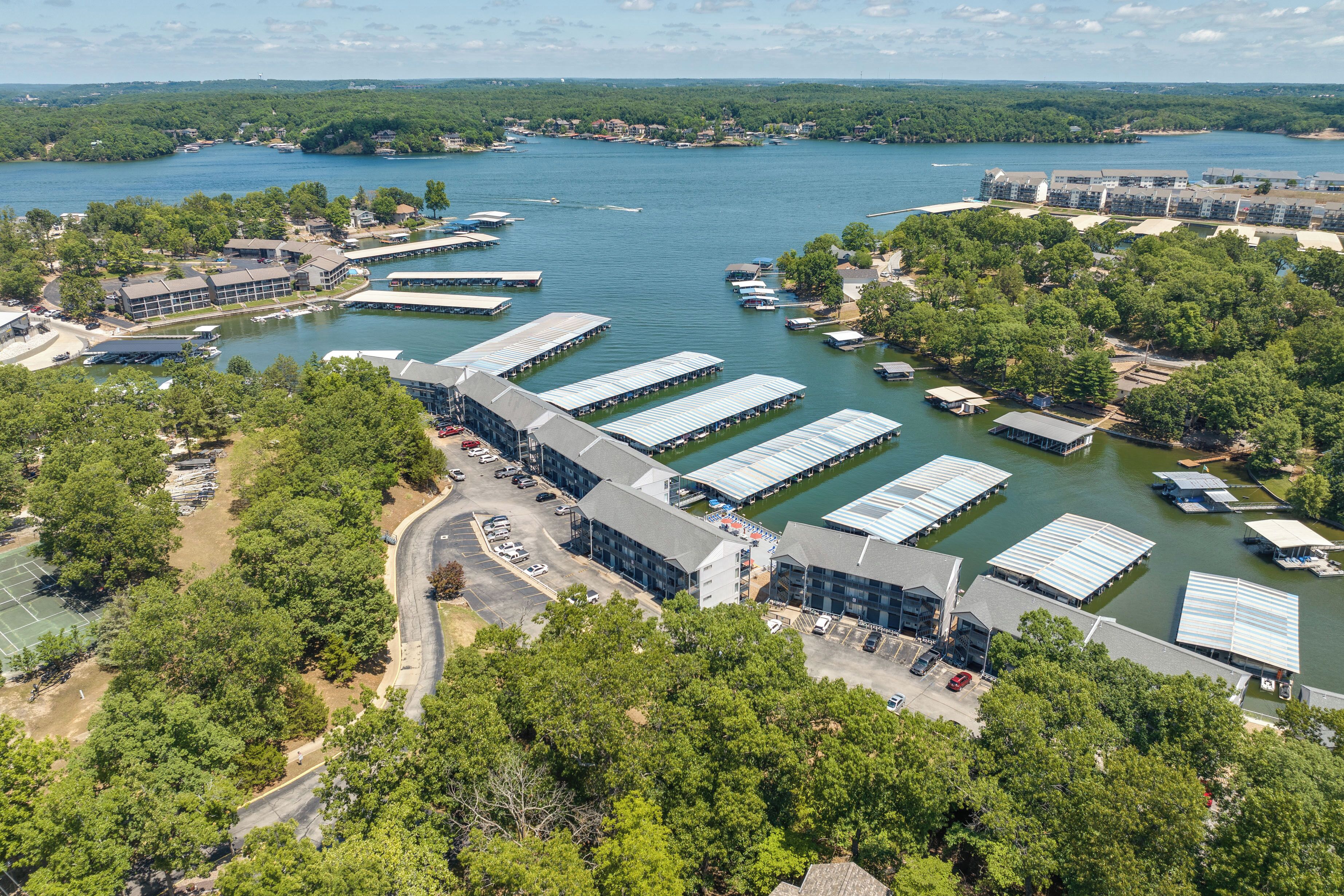 An aerial view of a marina with docked boats, a large building with a sloped roof, and surrounding greenery.