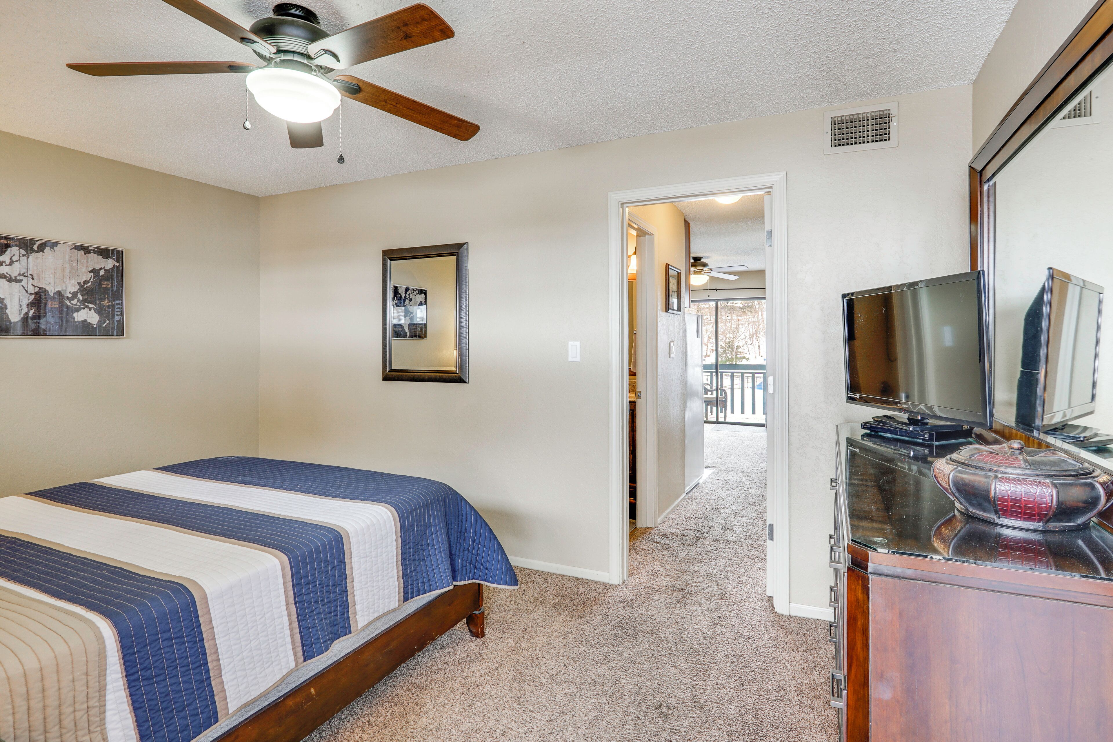 A bedroom with a bed, a ceiling fan, a dresser, and a television.