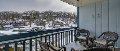 A balcony with wicker chairs and a table, overlooking a snowy residential area with houses and a dock.