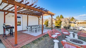 Eine überdachte Terrasse mit Grill, Esstisch, Stühlen und einem Feuerkorb.