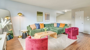 Ein modernes Wohnzimmer mit einem grünen Ecksofa, einem Holztisch, einem roten Sessel und einer Stehlampe.