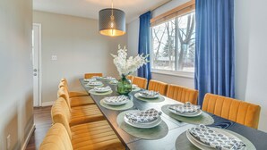 Ein Essbereich mit einem langen Tisch, gedeckt für sechs Personen, umrahmt von orangefarbenen Sesseln, einer Vase mit weißen Blumen und einer hängenden Leuchte.