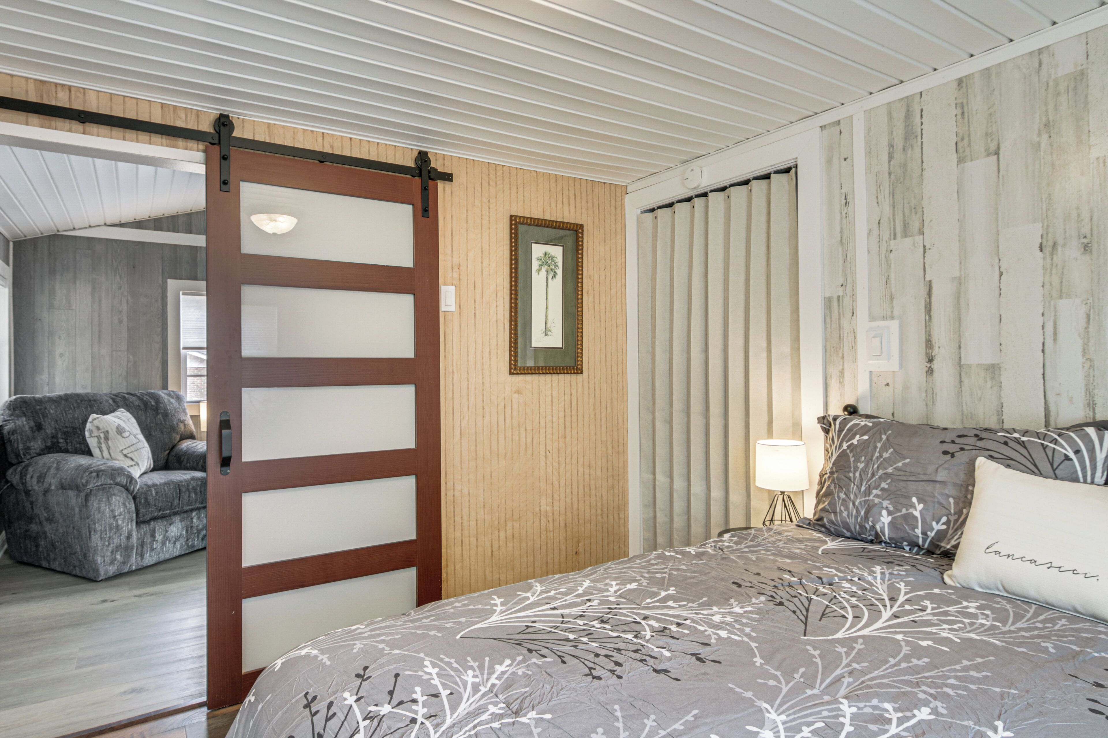 Un dormitorio con cama, sofá, puerta corredera y un cuadro en la pared.