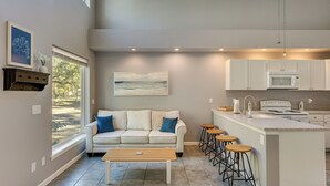 A modern kitchen with a central island, bar stools, and a dining area with a white sofa and coffee table. - < 1 Mi to St Johns River: Serene Family Home! (St. Augustine)