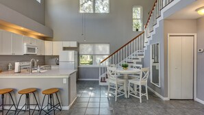 A modern kitchen with a central island, bar stools, and a staircase leading to an upper level. - < 1 Mi to St Johns River: Serene Family Home! (St. Augustine)