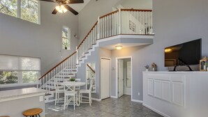 A spacious kitchen with a central island, white bar stools, a dining area with a round table, and a staircase leading to an upper level. - < 1 Mi to St Johns River: Serene Family Home! (St. Augustine)
