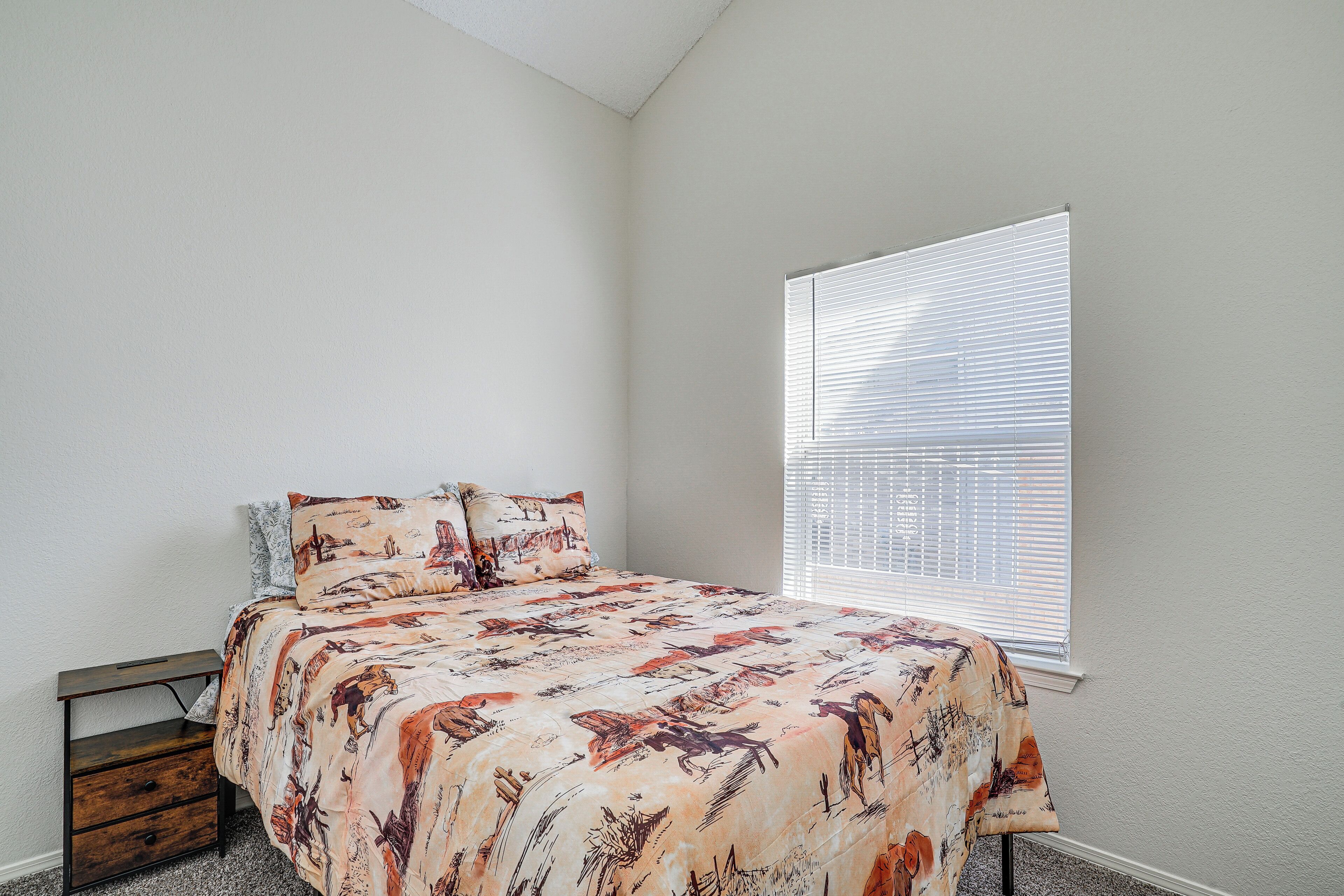 A bedroom with a bed, a nightstand, and a window with blinds.