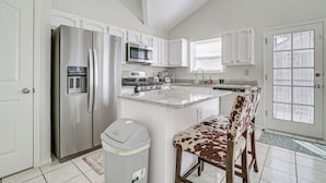 A kitchen with white cabinets, stainless steel appliances, a granite countertop island, and a cowhide chair. - Pool & Outdoor Space: Sunny El Paso Retreat! (El Paso)
