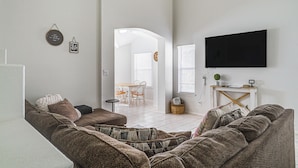 A living room with a sofa, a flat-screen TV mounted on the wall, and a dining area in the background. - Pool & Outdoor Space: Sunny El Paso Retreat! (El Paso)