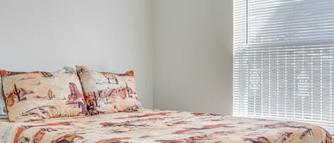 A bedroom with a bed, two pillows, and a window with blinds.