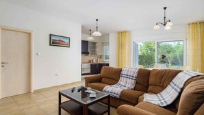 Ein Wohnzimmer mit braunem Sofa, einem Glastisch und einer Küche im Hintergrund.