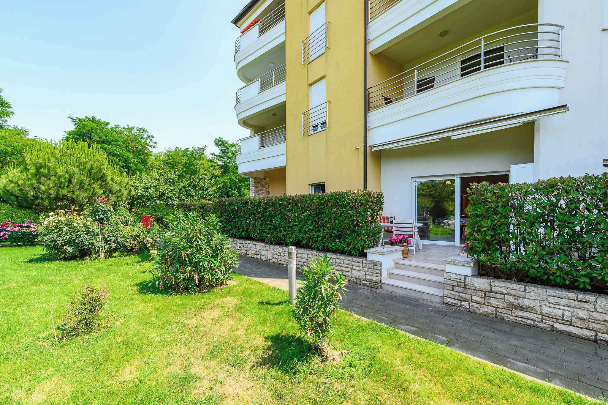 A multi-story residential building with balconies, a stone pathway, and a well-maintained garden.