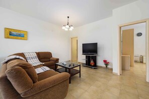 A living room with a brown sofa, a coffee table, a TV on a stand, a painting on the wall, and a door leading to another room. - Holiday apartment with air conditioning (Umag)