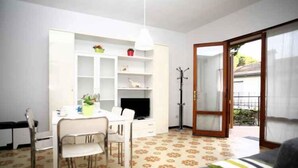 Espaço compacto com área de refeições, televisão, porta-casacos e porta de vidro deslizante para uma varanda.