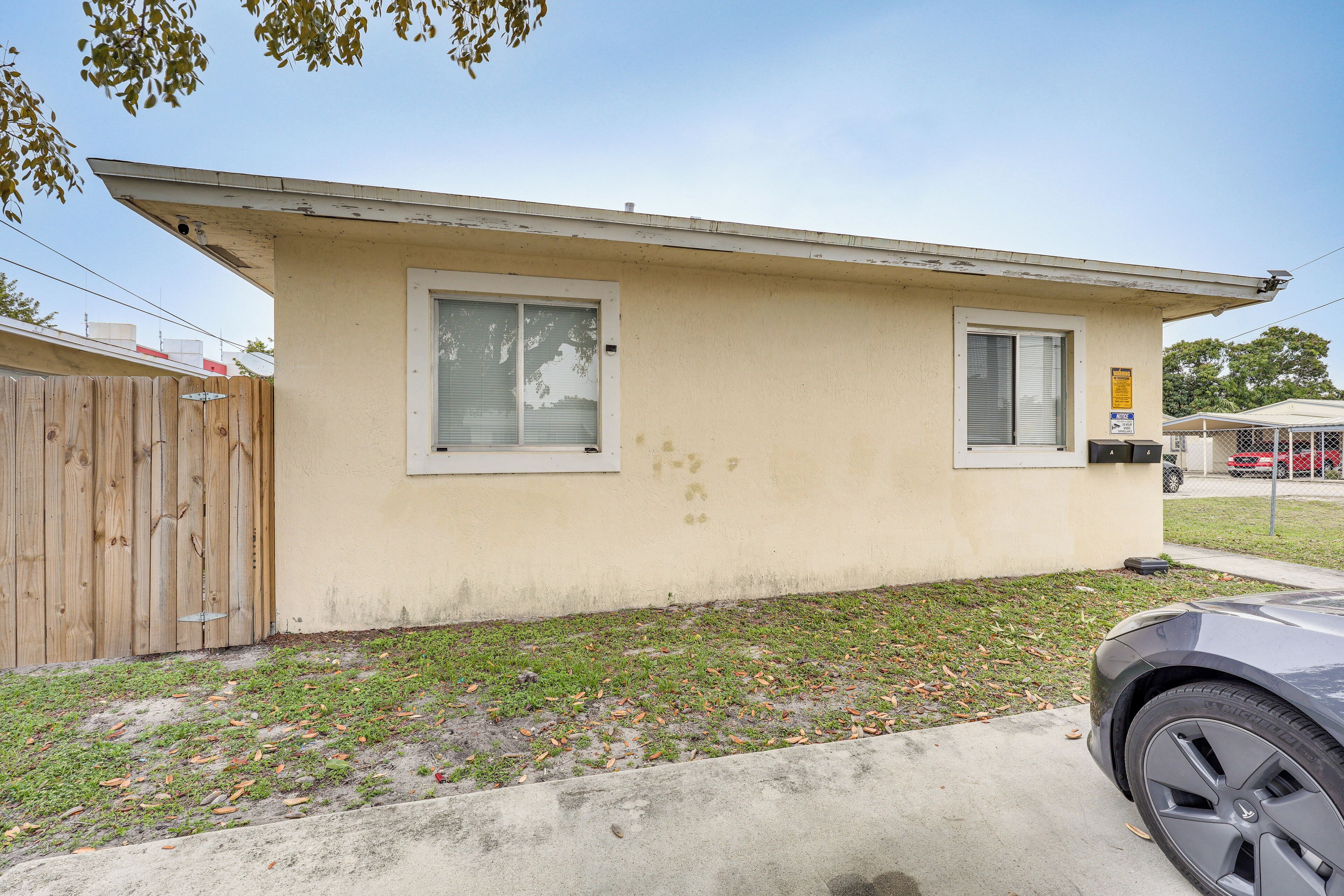 A single-story house with a small front yard, a wooden fence, and a parked car.