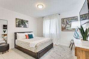 Quarto com cama, escrivaninha, cadeira, espelho e duas pinturas na parede.