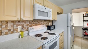 A kitchen with beige cabinets, a white stove, a microwave, and a refrigerator. - Apt Near Mall, The Big Easy Casino & Beaches! (Hallandale Beach)
