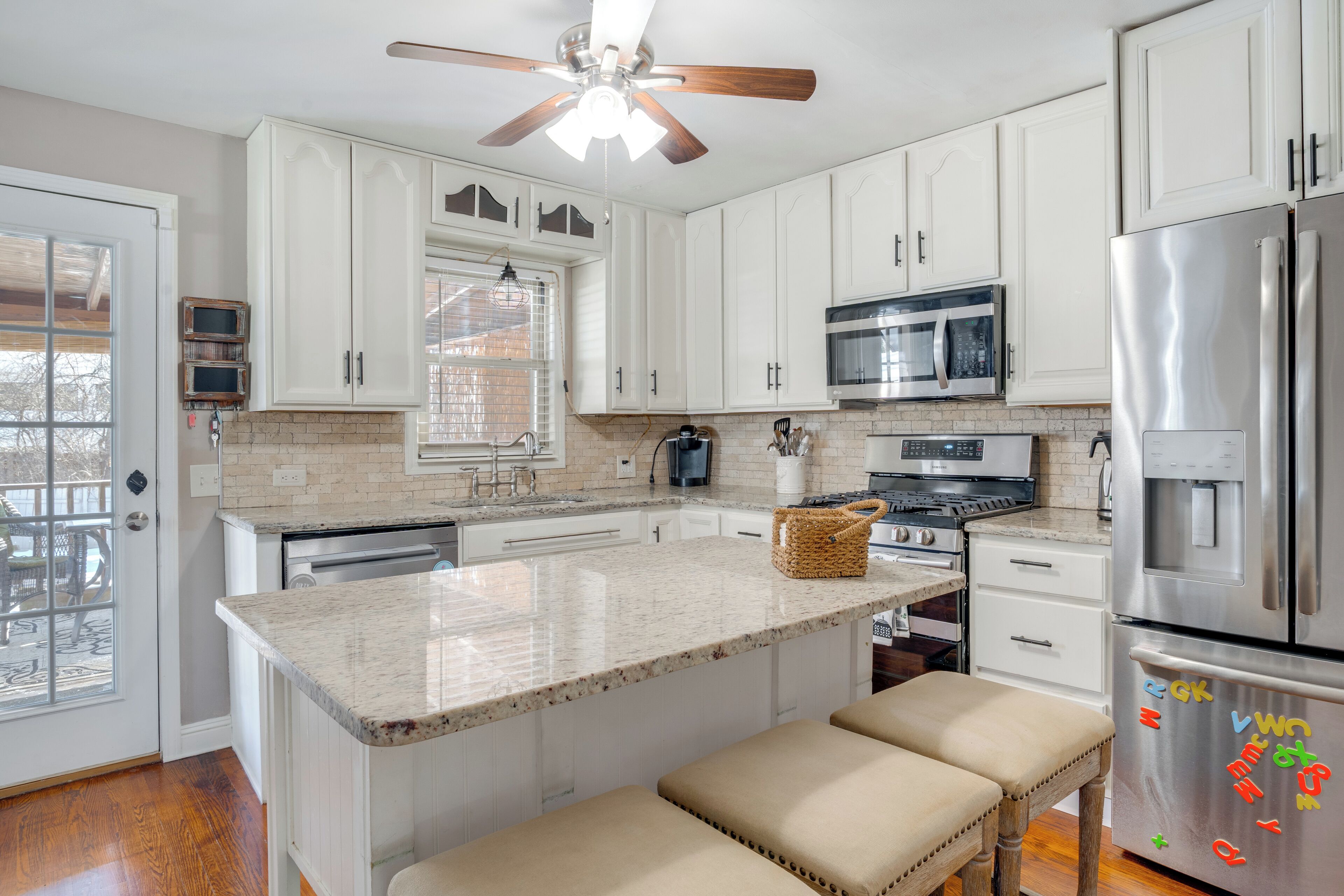 A kitchen with white cabinets, a granite countertop, a stainless steel refrigerator, and a ceiling fan.