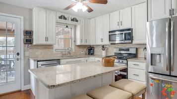 A kitchen with white cabinets, a granite countertop, a stainless steel refrigerator, and a ceiling fan.