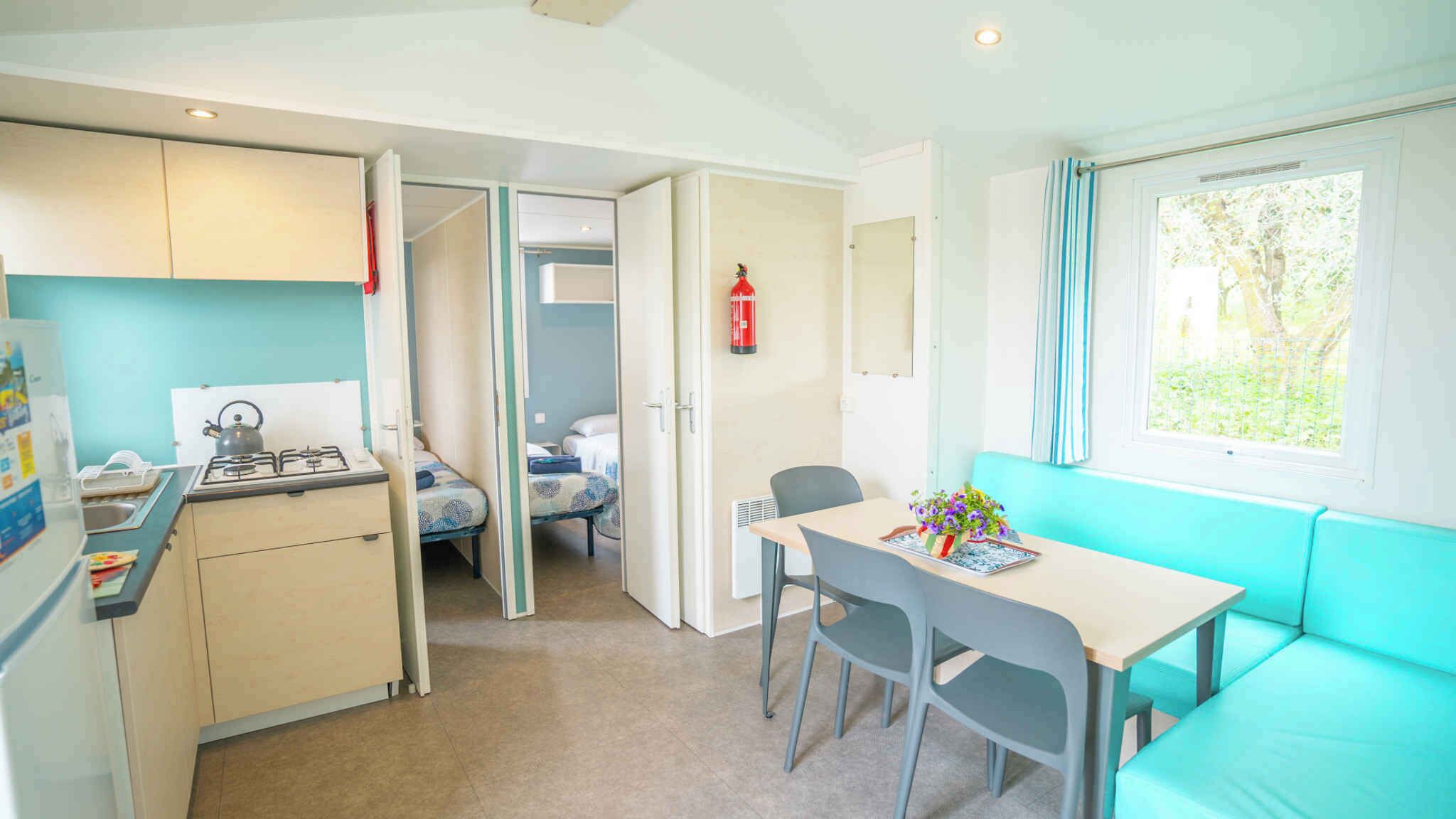 A compact kitchen with a gas stove, a small dining table with chairs, a kitchenette, and a window with a view of greenery.