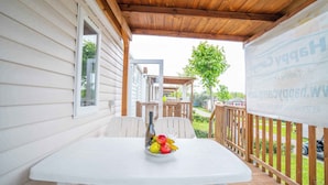 A covered patio with a table holding a fruit bowl, wooden deck, and a view of a residential area. - Mobile home with air conditioning, terrace and pool (Calella de la Costa)