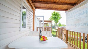 Eine überdachte Terrasse mit einem Tisch, auf dem sich eine Obstschale befindet, einem Holzboden und Blick auf ein Wohngebiet.