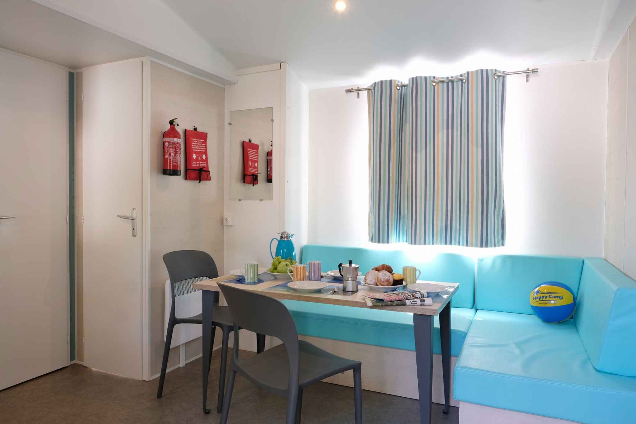 A small room with a blue sofa, a table with chairs, a window with striped curtains, and two fire extinguishers on the wall.