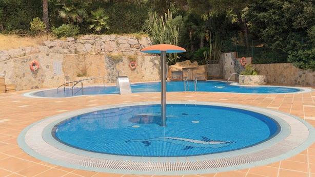 A swimming pool with a central fountain, surrounded by stone walls and a wooden deck. - Mobile home with air conditioning, terrace and pool (Calella de la Costa)