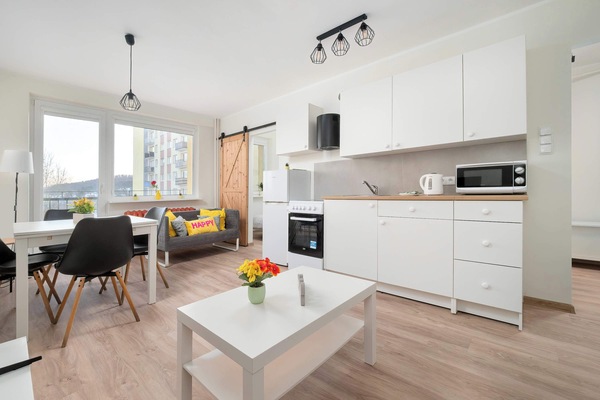 A wider angle of the open living area highlights a white coffee table and a compact dining space. Large windows bring in plenty of daylight, making the room feel airy and welcoming.