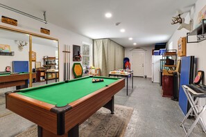 Una mesa de billar en una habitación con un espejo, una puerta y un piano.