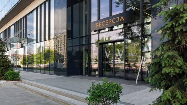Ein modernes Gebäude mit großen Glasfenstern und einem Schild mit der Aufschrift 'RECEPTJA'.