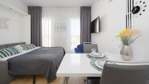 Ein modernes Hotelzimmer mit Bett, Schreibtisch, Fernseher und einer Vase mit Blumen.