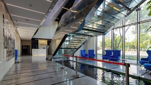 Ein modernes Interieur mit einer Glasstiege, einem Empfangstisch und blauen Sitzgelegenheiten neben einem Wasserspiel.