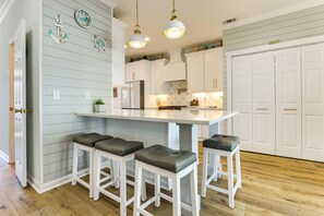 A kitchen with white cabinets, a central island with stools, pendant lighting, and decorative wall clocks. - 1 Mi to River! Relaxing Family Home in Bluffton (Bluffton)