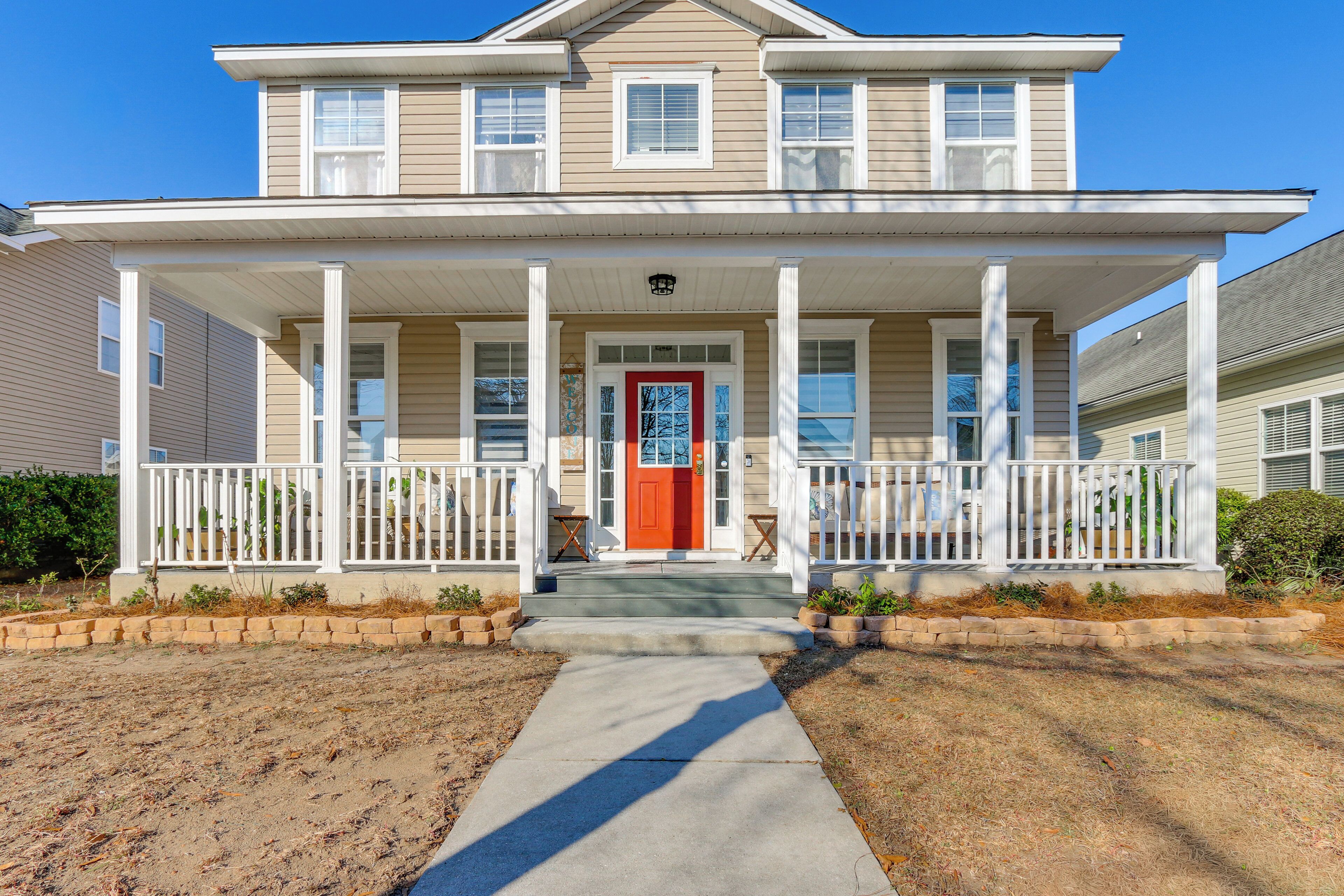 A two-story house with a front porch, a red door, and a small front yard.