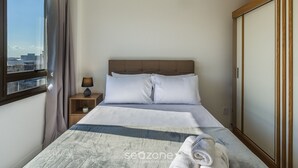 A hotel room with a bed, a nightstand, a lamp, a view of the city, and a wardrobe. - Full Studio 700m From Bourbon Shopping Umb0604 (Porto Alegre)