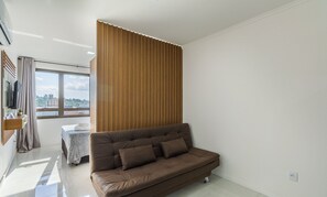 Een moderne woonkamer met een bruine bank, een wand van houten panelen en een raam met uitzicht op de stad.