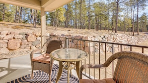 A covered outdoor seating area with wicker furniture and a glass table, overlooking a forested landscape. - Trail Access On-site! Wooded Colorado Springs Gem (Colorado Springs)