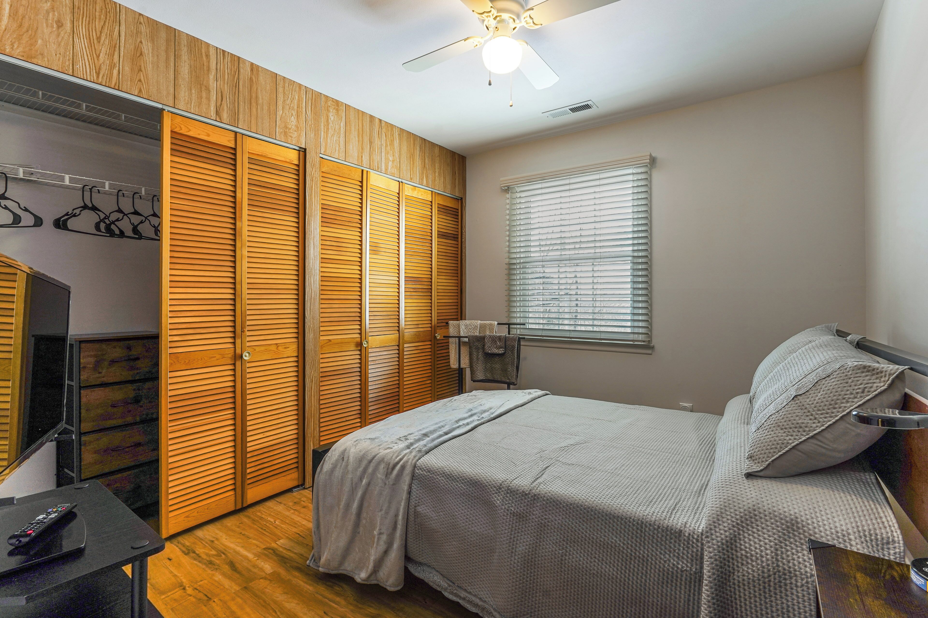 A bedroom with a bed, wooden wardrobe, and a ceiling fan.