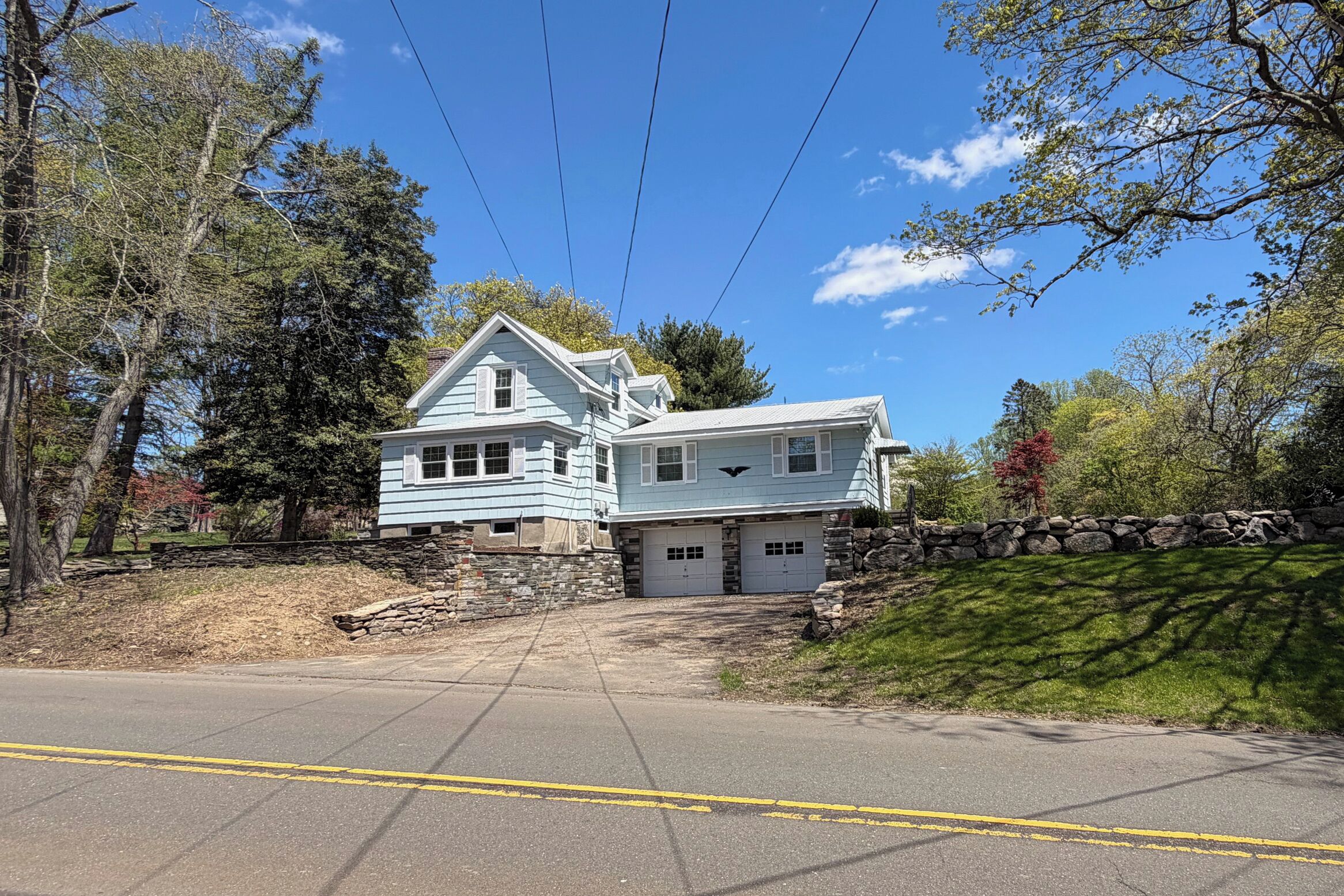 A two-story house with a stone wall, a garage, and a driveway.