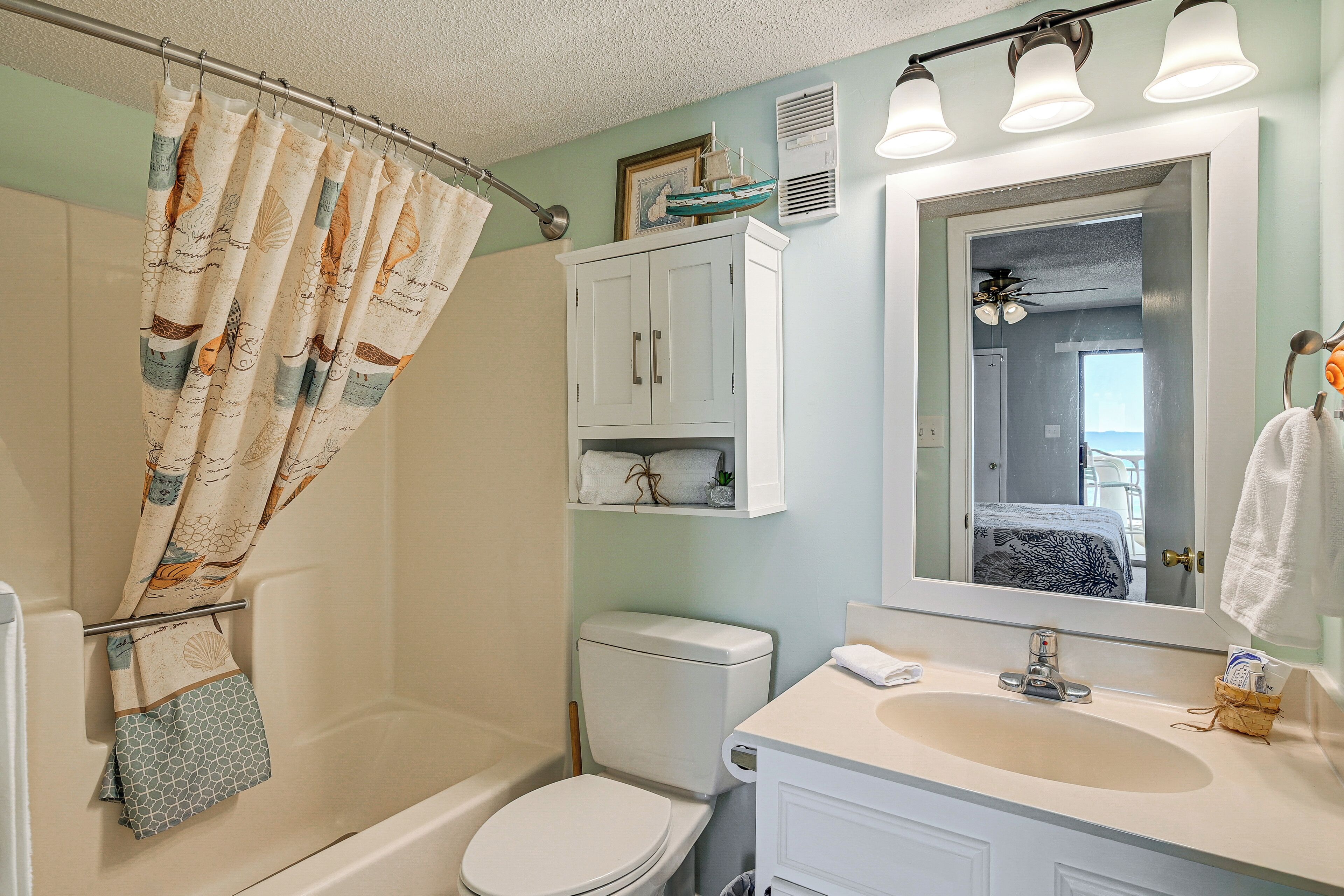 Une salle de bain avec un rideau de douche, des toilettes, un lavabo et un miroir.