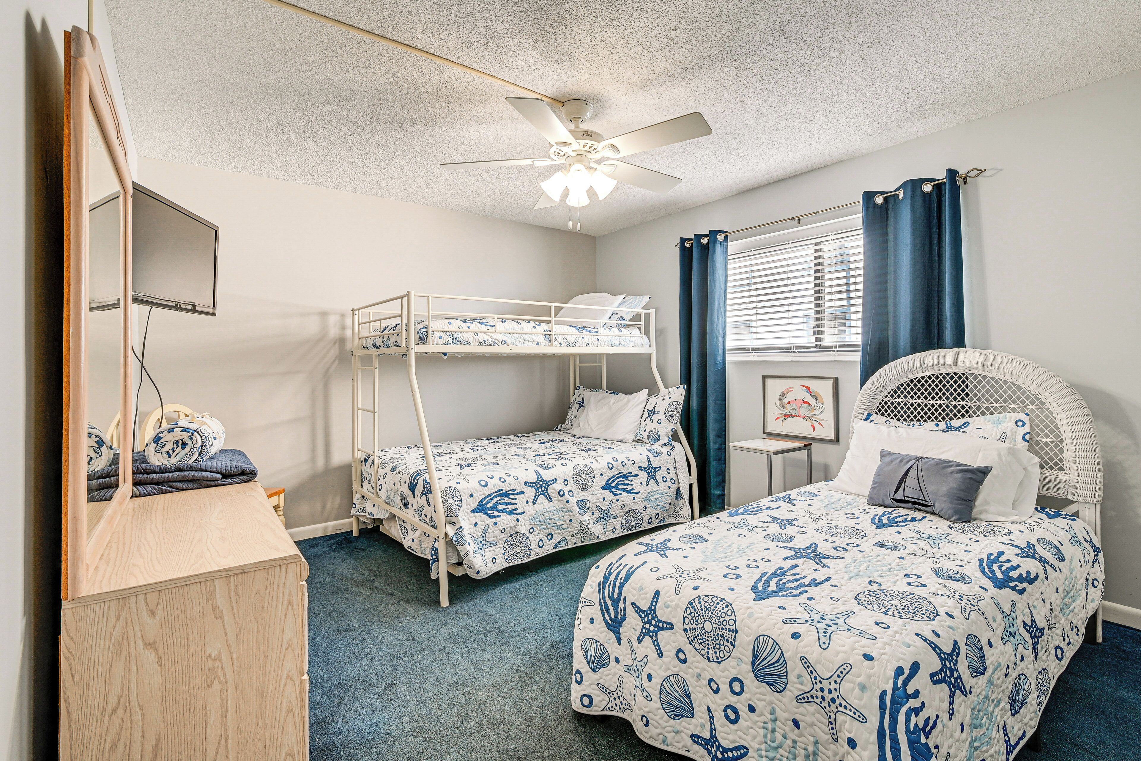 Une chambre avec des lits superposés, un ventilateur de plafond, une commode et une fenêtre avec des rideaux.