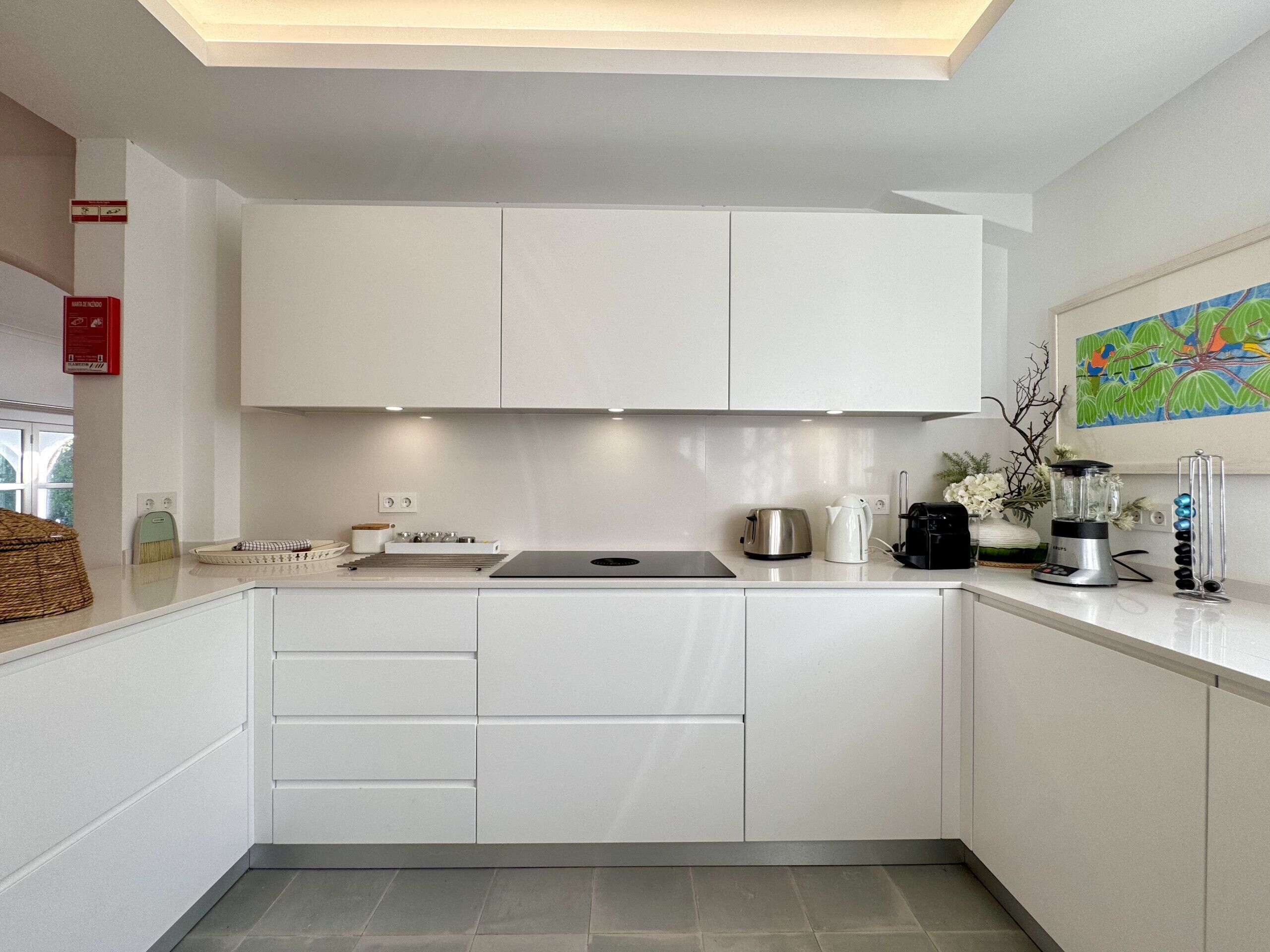 A modern kitchen with white cabinets, a stainless steel kettle, a coffee maker, and a blender on the counter.