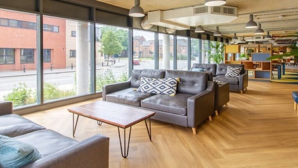 A spacious lobby with leather sofas, a wooden coffee table, and pendant lighting. Large windows offer views of the street and buildings outside. - Cathedral Road by UTDM (Derby)
