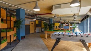 A modern indoor space with a foosball table, wooden shelving with plants, and pendant lighting. - Cathedral Road by UTDM (Derby)